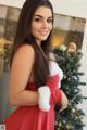 A woman in a red dress standing next to a Christmas tree.