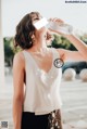 A woman in a white top drinking water from a bottle.