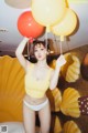 A woman in a yellow bikini holding a bunch of balloons.